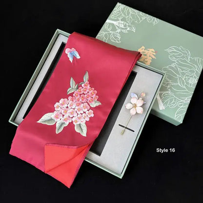 Red fabric with floral embroidery and a brooch in a decorative box on a black background