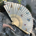 Handheld fan with butterfly designs on a stone surface