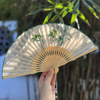 Handheld fan with bamboo design held by a hand against a blurred natural background