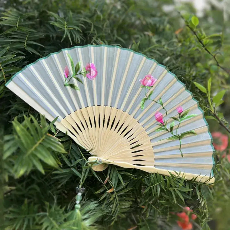 Handheld fan with floral design on a green leafy background