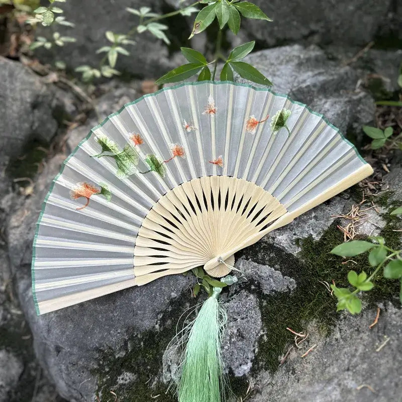 Decorative fan with floral design on a stone surface with greenery