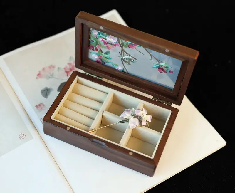 Wooden jewelry box with floral design on lid, containing a brooch and ring holder.