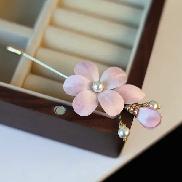 Pink flower-shaped hairpin with pearl details on a blurred jewelry box background