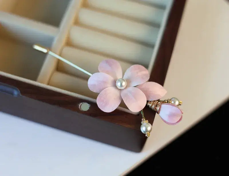 Pink flower-shaped hairpin with pearl details on a blurred jewelry box background