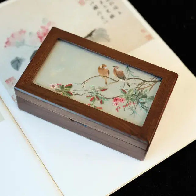 Wooden box with a decorative glass lid featuring birds and flowers on a floral-patterned surface.