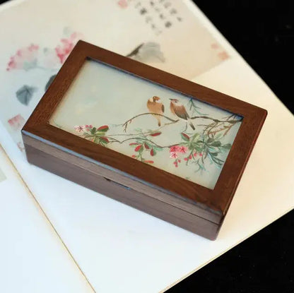 Wooden box with a decorative glass lid featuring birds and flowers on a floral-patterned surface.