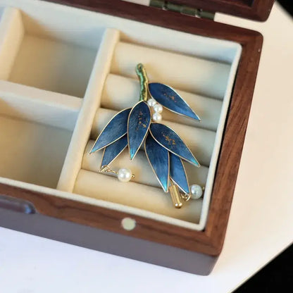 Blue leaf-shaped brooch with gold accents and pearls in a jewelry box