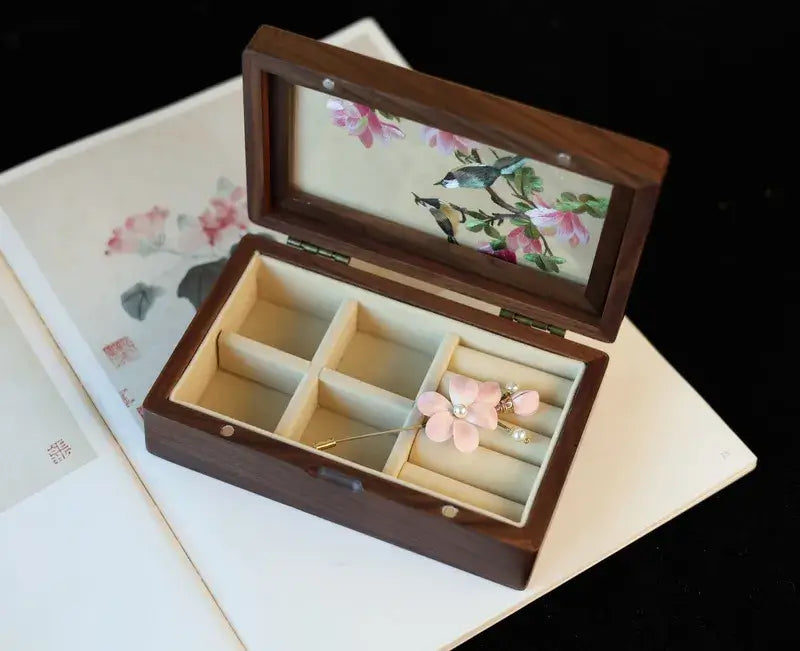 Wooden jewelry box with floral design on lid and interior, containing a pink flower-shaped earring.