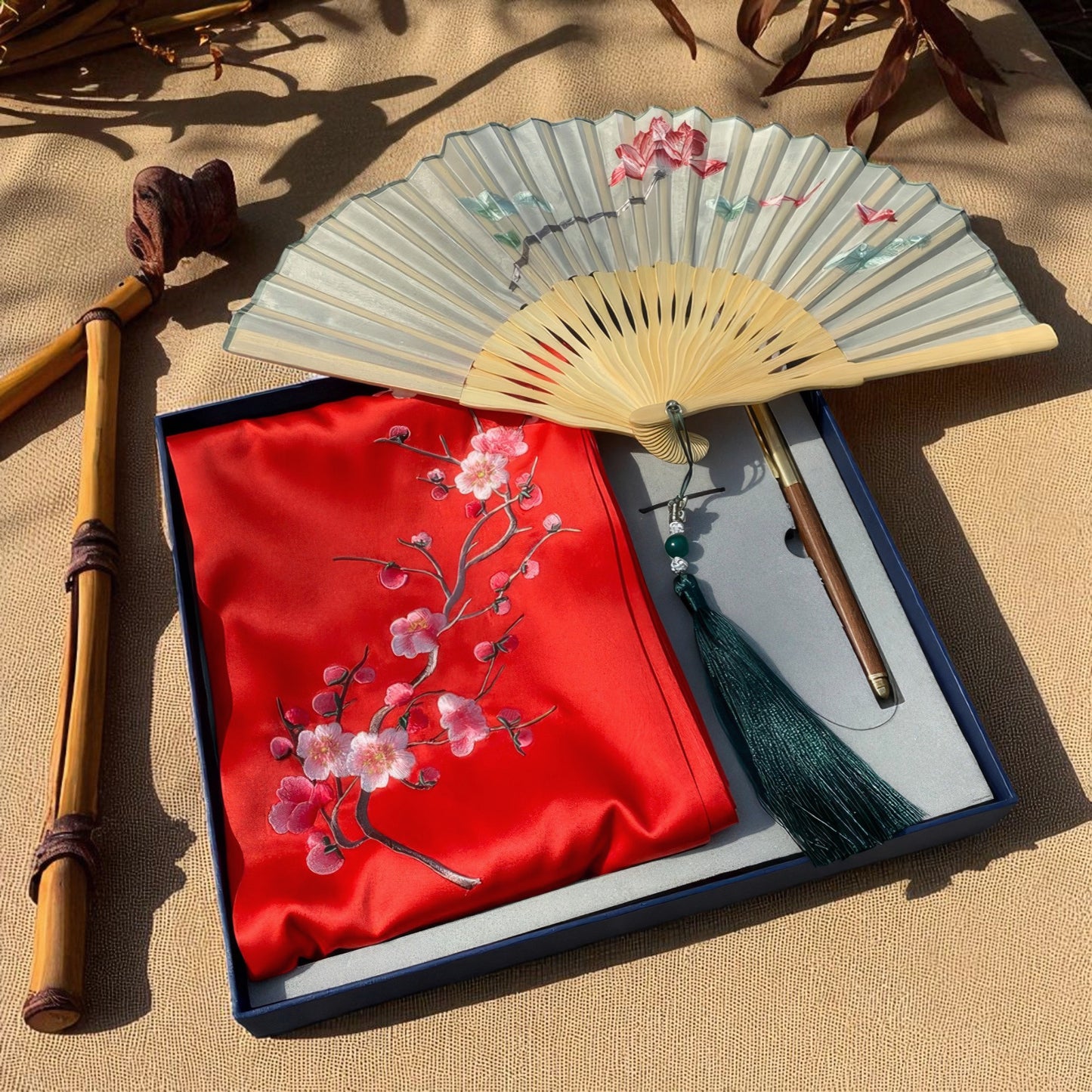Traditional folding fan with floral design on a red fabric cover, set against a beige background.