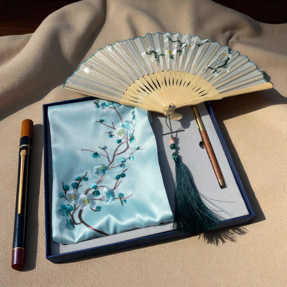Embroidered blue pouch with floral design, wooden fan, and brush on a beige fabric background