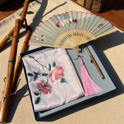 Embroidered fabric with floral design, fan, and bamboo sticks on a textured surface