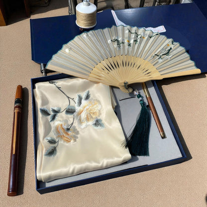 Embroidered fabric with floral design, fan, and pen on a blue surface.