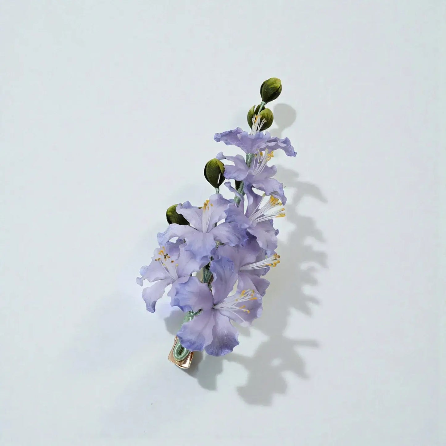 Floral hair clip with purple flowers and green leaves on a light gray background