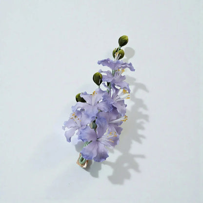 Floral hair clip with purple flowers and green leaves on a light gray background