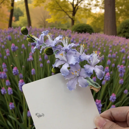 Hand holding a white card with a purple flower in front of a field of purple flowers.