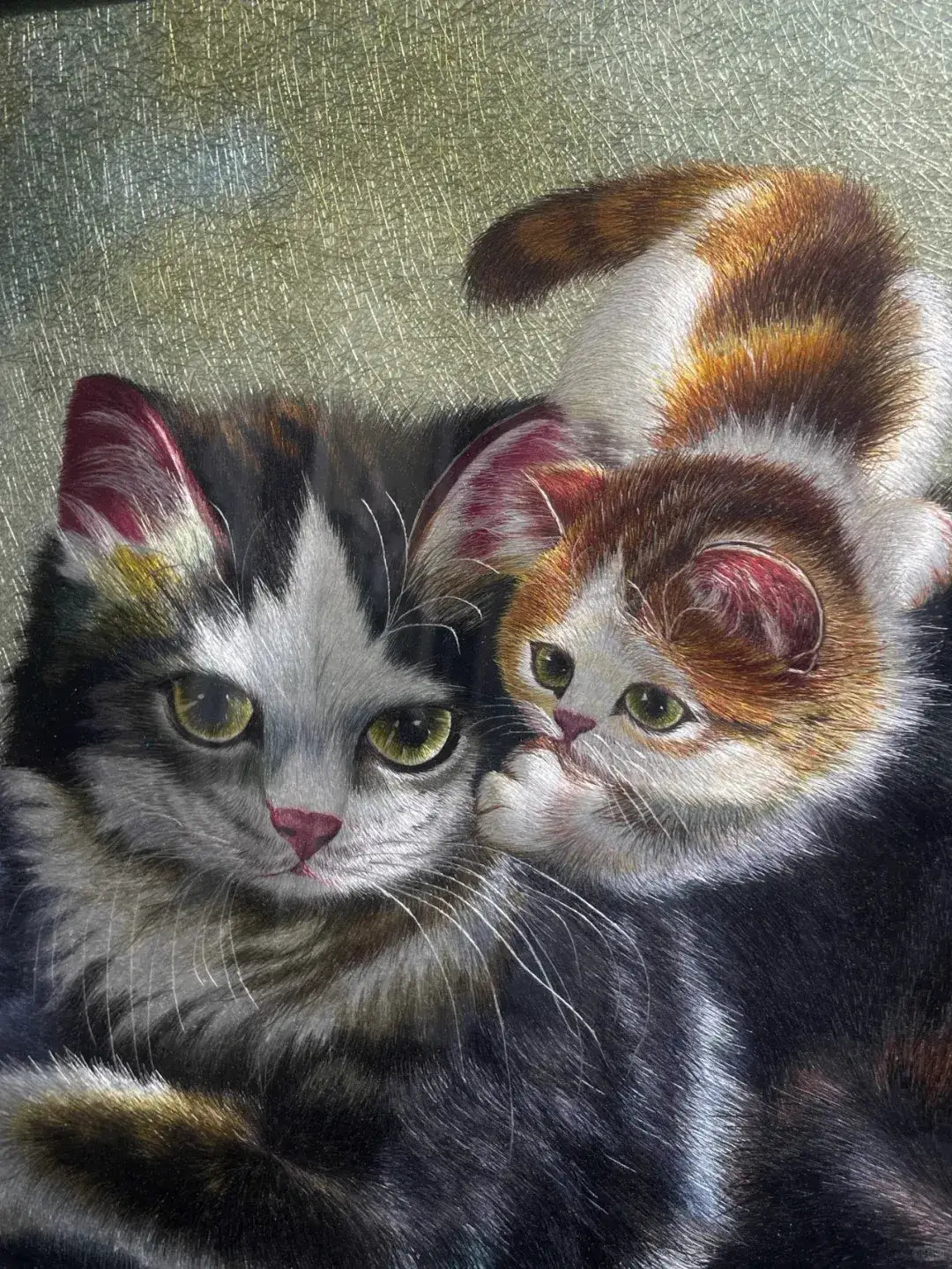 Two kittens with calico fur pattern on a textured fabric background