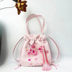 Pink drawstring bag with floral embroidery and tassel on a white background