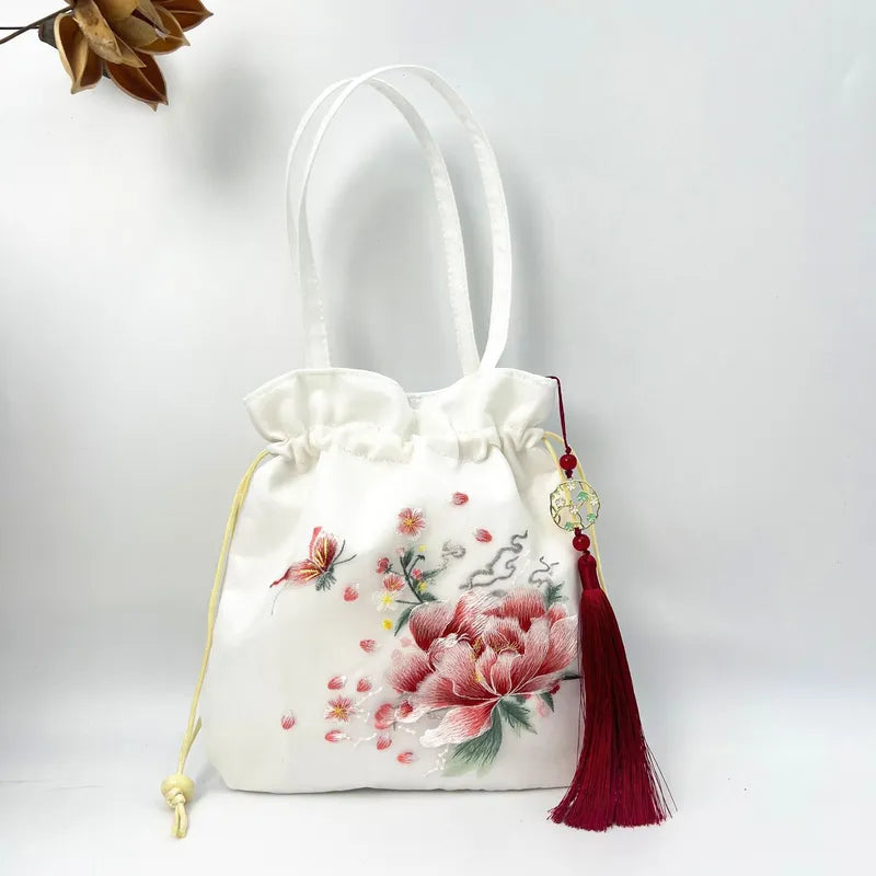 White drawstring bag with floral design and red tassel on a white background