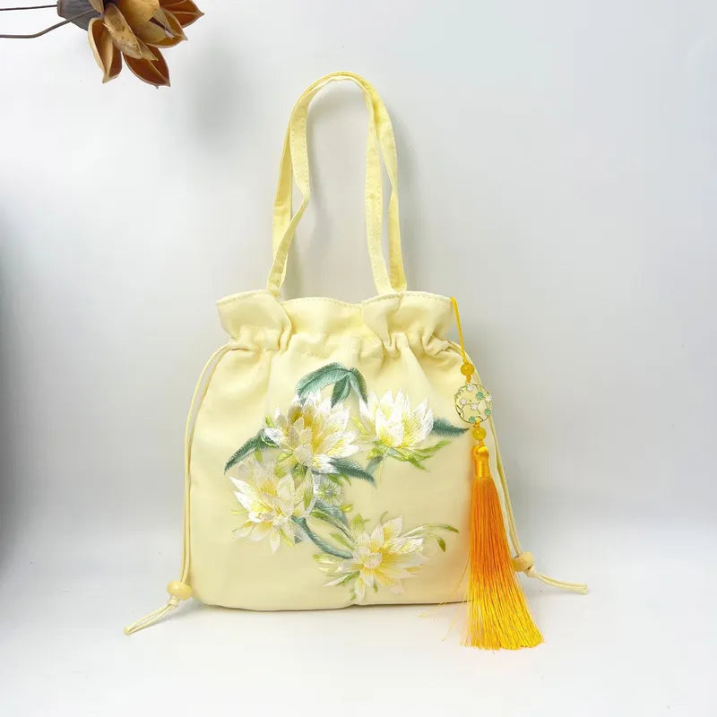 Yellow drawstring bag with floral embroidery and a tassel on a light gray background