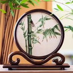 Decorative plate with bamboo design on a wooden stand, surrounded by greenery.