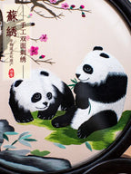 Embroidery of two pandas on a circular frame with floral decorations.