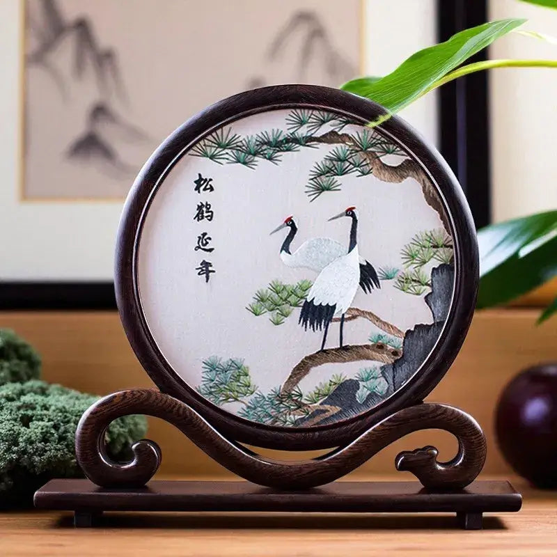 Decorative plate with cranes and Chinese characters on a wooden stand, with a blurred background.