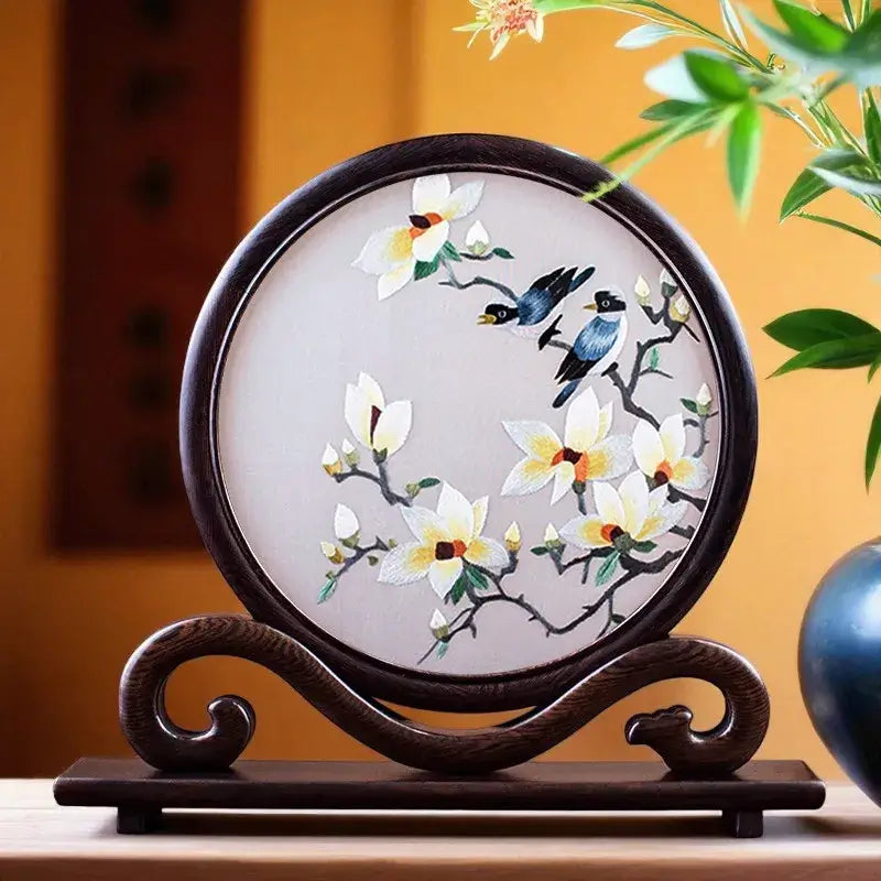 Decorative piece with floral and bird design on a wooden stand against a warm background