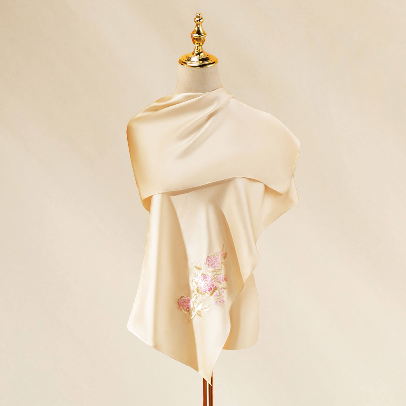 Beige scarf with floral embroidery on a mannequin against a beige background