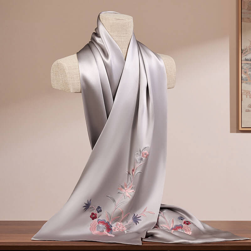 Silver scarf with floral embroidery on a mannequin against a beige wall.