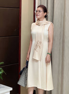 Woman in a light-colored dress with a scarf, standing indoors against a neutral background.