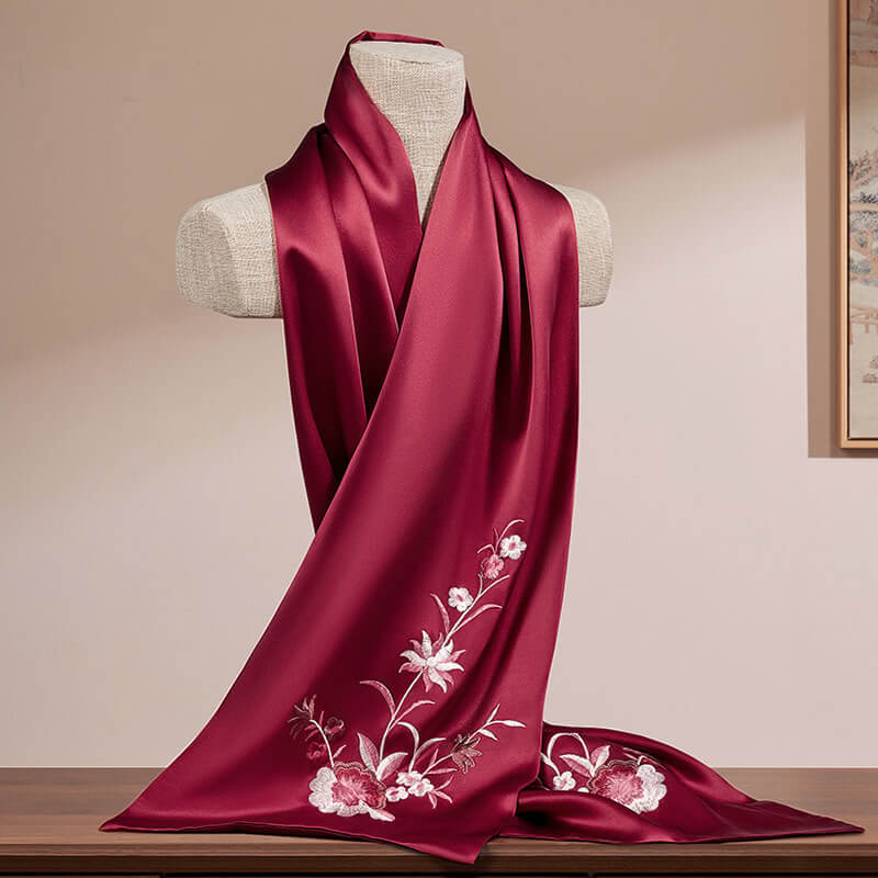 Red silk scarf with floral embroidery on a mannequin against a beige wall.