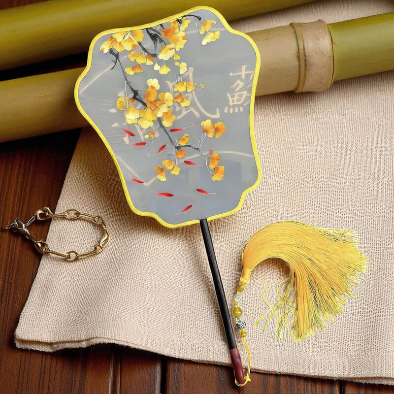 Decorative fan with yellow tassel and floral design on a textured surface