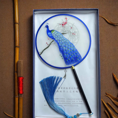 Decorative fan with peacock design in a box on a brown background