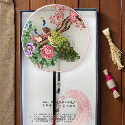 Decorative round fan with peacocks and flowers on a wooden surface
