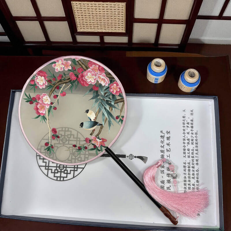 Decorative fan with floral design and tassel on a wooden surface