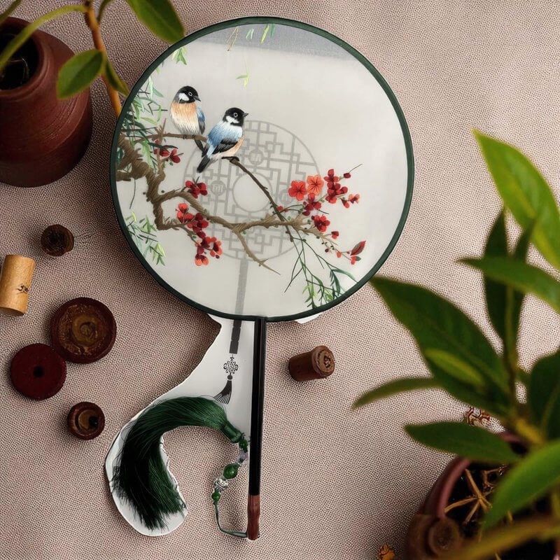 Handheld fan with bird and floral design on a textured surface