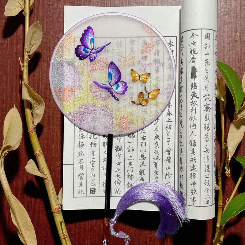 Decorative fan with butterfly design on a wooden surface with calligraphy