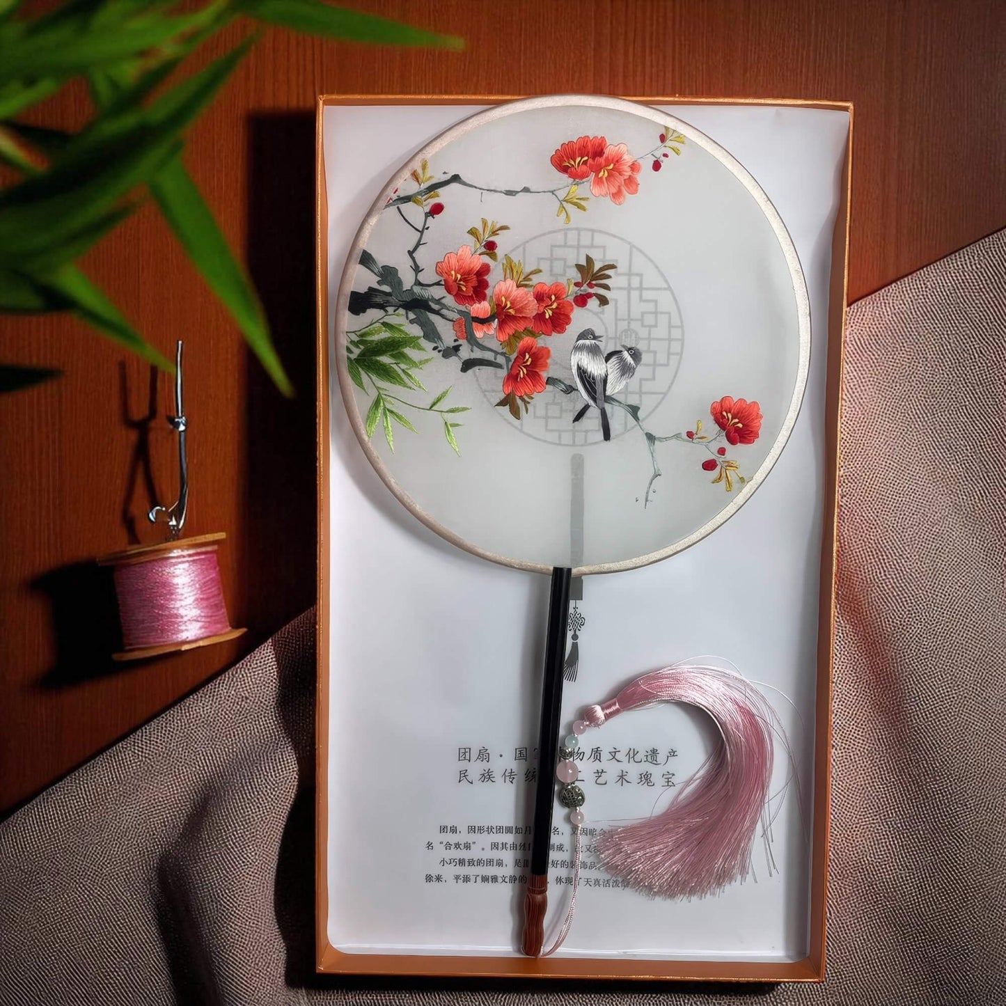 Decorative fan with floral design in a box on a wooden surface