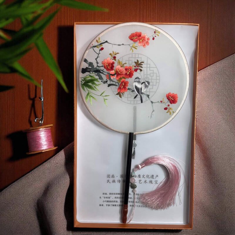 Decorative fan with floral design in a box on a wooden surface