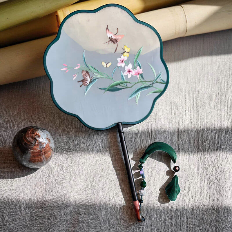 Decorative hand fan with floral and butterfly design on a textured surface