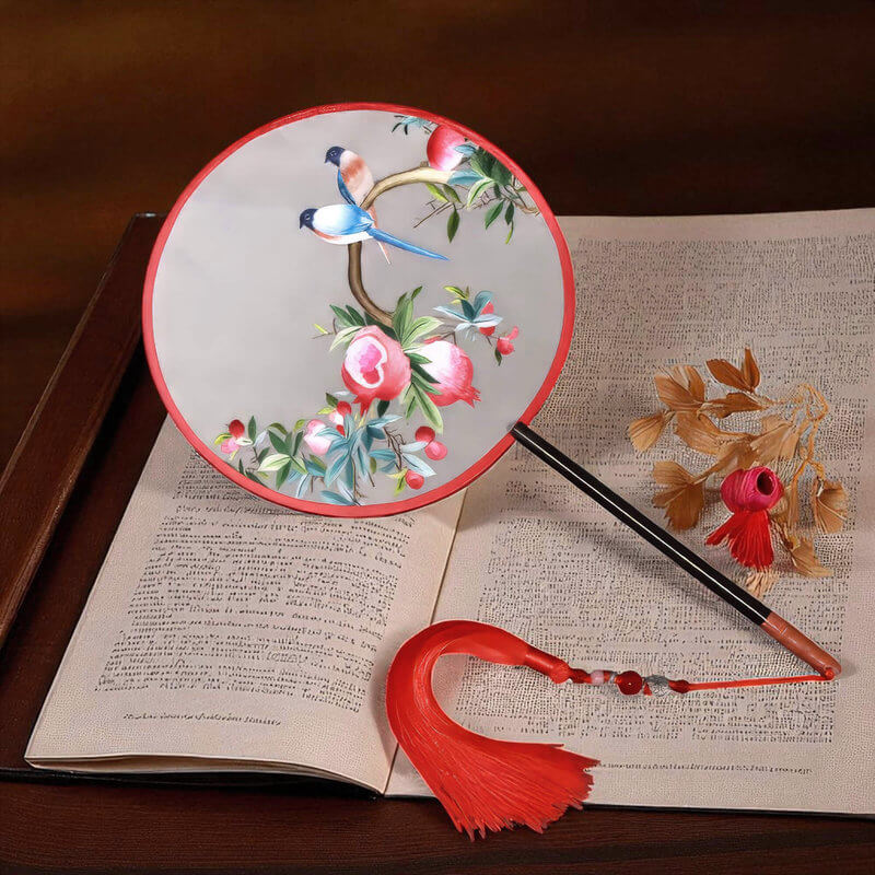 Decorative fan with floral and bird design on an open book