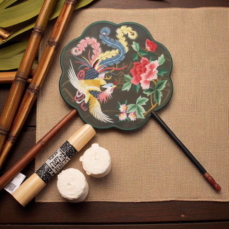 Decorative fan with floral and bird design on a textured surface with bamboo and white items.
