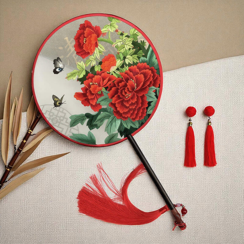 Decorative fan with red floral design and tassels on a beige background