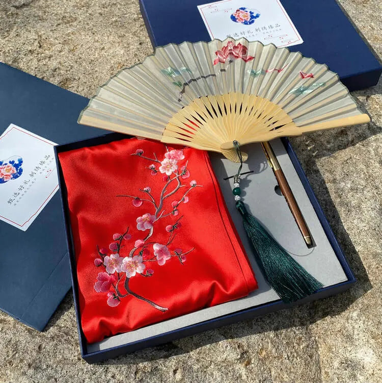 Decorative fan with floral design on a red fabric cover, displayed in an open box.