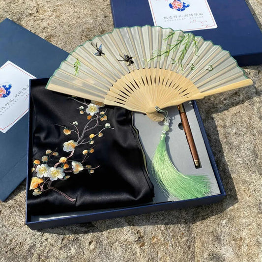 Decorative fan with floral design on a black fabric cover in a box.