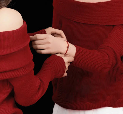Two people wearing red sweaters holding hands against a black background