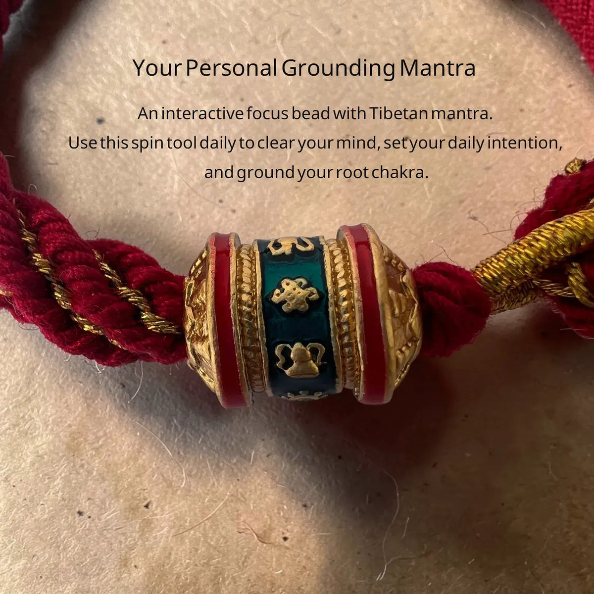 Decorative bead with Tibetan mantras on a red cord, placed on a textured surface.