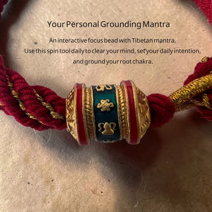 Decorative bead with Tibetan mantras on a red cord, placed on a textured surface.