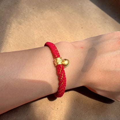 Red bracelet with a gold heart charm on a wrist against a neutral background