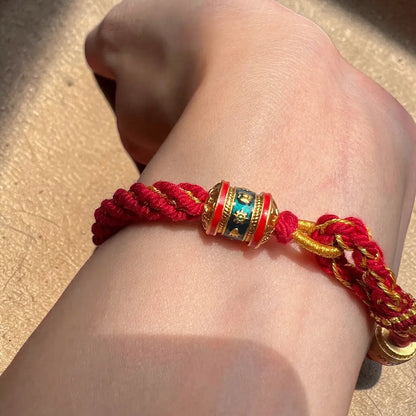 Red and gold bracelet with a colorful bead on a wrist against a neutral background